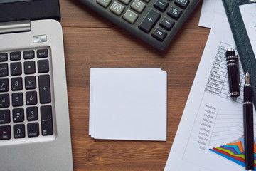 Financial printed paper charts, graphs, diagrams, computer, pen, and calculator on wooden desk.
