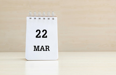 Closeup surface note book with black 22 mar word in page on blurred brown wood desk and wood wall textured background with copy space under window light