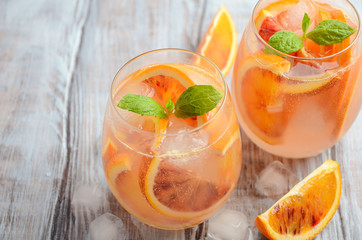 Cold refreshing drink with blood orange slices in a glass on a wooden background. Selective focus, copy space.