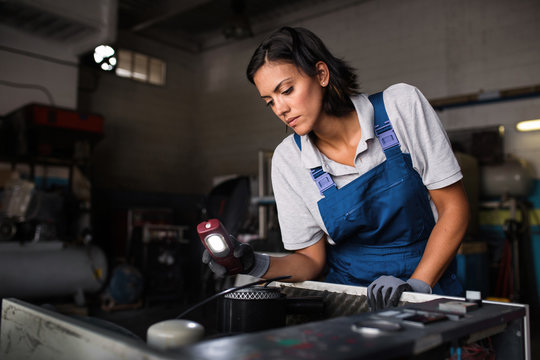 female mechanic looking for a fault on a compressor engine using a flashlight