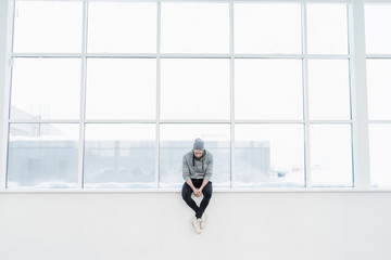 Young man sitting against of big glass window with white geometric lines