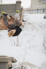 Teenager blonde hair guy training parkour jump flip in the snow covered park
