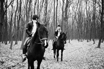 Young stylish couple riding on horses at autumn forest.  Black and white photo.