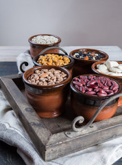 Assortment of beans in brown bowls on wooden background. Soybean, red kidney bean, black bean,white bean, red bean and brown pinto beans