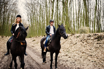 Young stylish couple riding on horses at autumn forest.