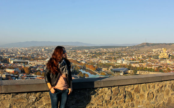 Girl in the sunglass looks. Panoramic view of old Tbilisi, Georgia at the background. Traveler woman walking around the city by looking at the view from above. The view from the castle Narikala.