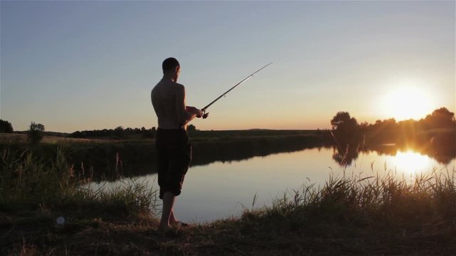 Man Fishes With Spinning At Sunset/man standing on the lake at sunset with fishing rod