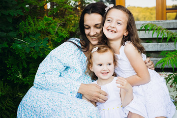 Cheerful little girls lean to their mother sitting outside