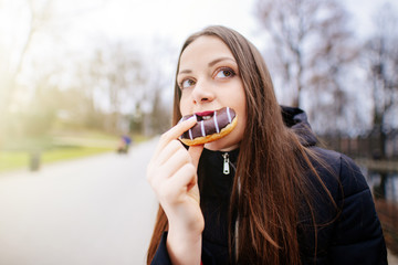 Young pretty girl eating donut at park background and smile