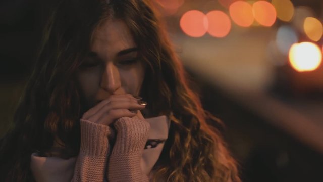 Woman warming hands at night road traffic background