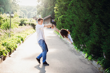 Father whirls little daughter on path along green bushes