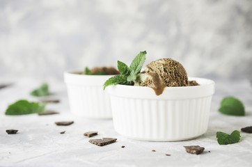 chocolate mint ice cream in white bowls with pieces of chocolate and mint leaves on a marble table