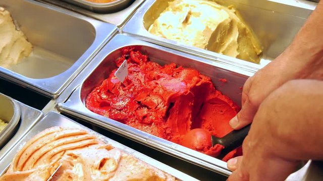 4K close-up of the hand of a man dipping a spoon in a red scoop ice-cream, blackcurrant, strawberry and raspberry flavor. 