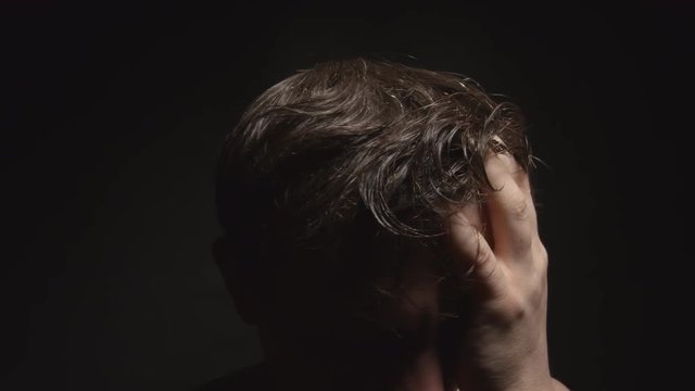 Worried man touches his wet hair by hand in dark room