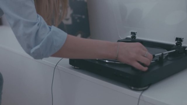 HANDHELD FOLLOW young happy Caucasian teen playing a record on a vinyl turntable, then putting on headphones and dancing at home. 4K UHD RAW edited