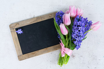 Pink tulips and blue hyacinths flowers bouquet on white wooden table with blackboard