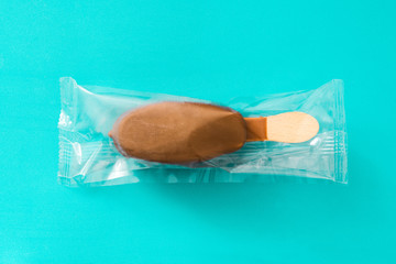 Chocolate ice cream popsicle wrapped in plastic bag, isolated on blue background.
