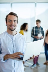 Man using laptop while colleagues discussing in background