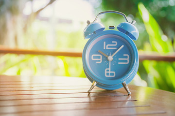 Blue alarm clock on a wooden desk with nature background, close up blue alarm clock