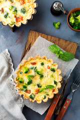 Homemade quiche tart with red fish salmon, broccoli, basil, seasonings and cheese on a gray stone background. Selective focus.Top view.