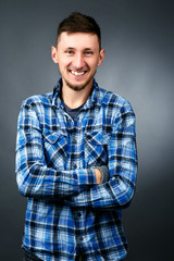 Handsome smiling man in blue plaid shirt crosses his hands on chest