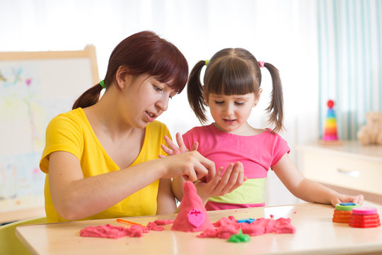 Child girl and mother playing with kinetic sand at home