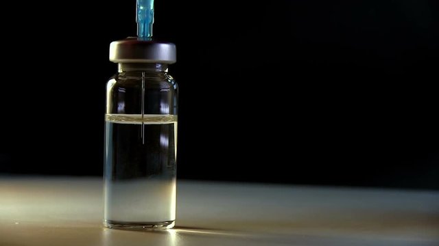 Doctor Recovers Vaccine In Syringe From Glass Ampoule Bottle With Medication On Dark Background