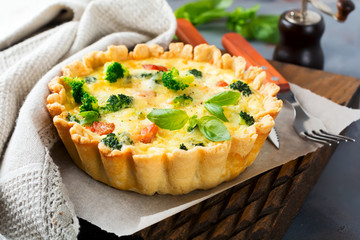 Homemade quiche tart with red fish salmon, broccoli, basil, seasonings and cheese on a gray stone background. Selective focus..