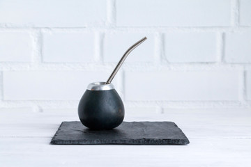 Traditional calabash gourd for mate tea drinking with straw on slate / white table. Copy space.