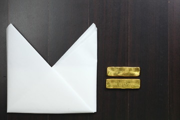 The white color paper napkin on the dark color wooden dining table floor and gold bar represent the...