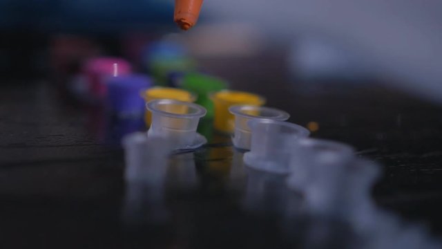 Close up shot of tattoo master dropping color ink into the container in slow motion.