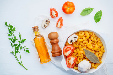 Italian foods concept and menu design . Pasta elbow macaroni  with ingredients sweet basil ,tomato ,garlic ,extra virgin olive oil ,parsley ,bay leaves and champignon  on white background  flat lay .