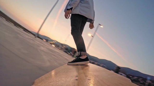 Cool guy skates on his long wooden longboard at sunset evening time, bottom low view behind from board level