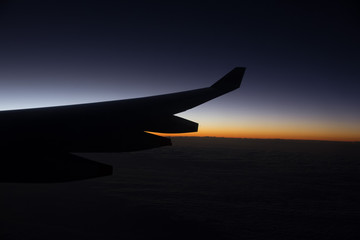 Fototapeta premium Silhouette of airplane wing up in the sky with beautiful horizon during sunrise. Noise due to low light condition.