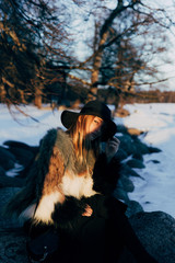 Portrait of a young beautiful blonde woman with hat, in a fur coat, outside, on the snow. A good dark day with beautiful shadows - a sunny winter day, sunset.