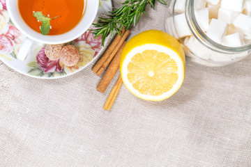 Cup of black or red tea with lemon, rosemary, mint, cinnamon sticks, sugar on grey tablecloth, top view