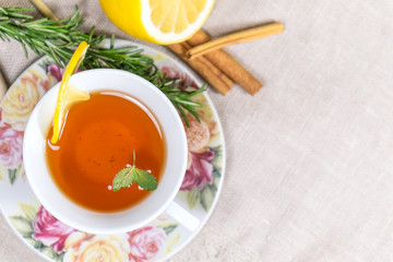 Cup of black or red tea with lemon, rosemary, mint, cinnamon sticks, sugar on grey tablecloth, top view
