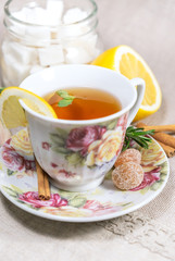 Cup of black or red tea with lemon, rosemary, mint, cinnamon sticks, sugar on grey tablecloth