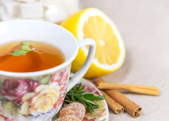 Cup of black or red tea with lemon, rosemary, mint, cinnamon sticks, sugar on grey tablecloth