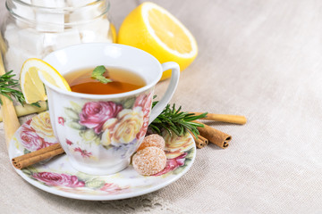 Cup of black or red tea with lemon, rosemary, mint, cinnamon sticks, sugar on grey tablecloth