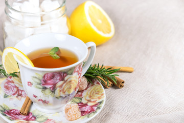 Cup of black or red tea with lemon, rosemary, mint, cinnamon sticks, sugar on grey tablecloth