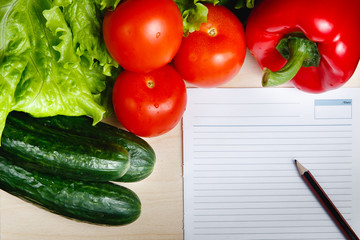 Fresh vegetables on the table: red pepper, lettuce, cucumber, tomatoes, sheet for notes - notepad. Cutting board