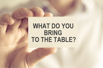 Businessman holding WHAT DO YOU BRING TO THE TABLE ? message card