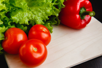 Fresh vegetables on the table: red pepper, lettuce, cucumber, tomatoes. Cutting board