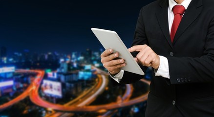 smart businessman in suit using his tablet, business and technology concept on blurred night city background,copy space, color tone effect, wide screen