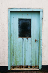 Rustic wooden door, with pale blue peeling paint  set in a white wall.