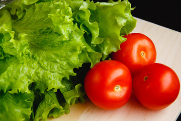 Fresh vegetables on the table:  lettuce,  tomatoes. Cutting board