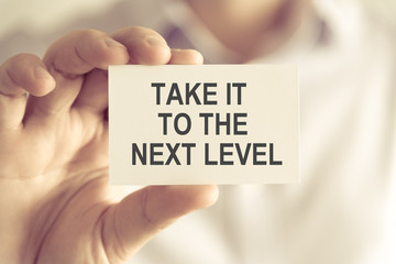 Businessman holding TAKE IT TO THE NEXT LEVEL message card