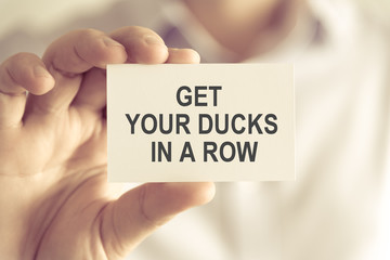 Businessman holding GET YOUR DUCKS IN A ROW message card