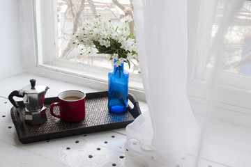 Cup of coffee with a blue vase on a wooden tray near the window